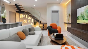 A modern living room with a white sofa, orange armchair, and a flat-screen TV mounted on the wall. - Chennad Apartment  (Abuja)