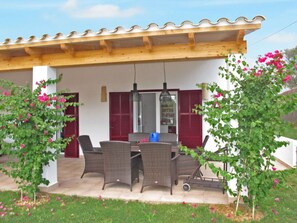 Une terrasse couverte, aménagée avec des meubles en osier, une table à manger et des volets rouges.