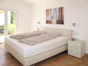 Une chambre à coucher avec un lit, une table de chevet, une lampe fixée au mur et une fenêtre.