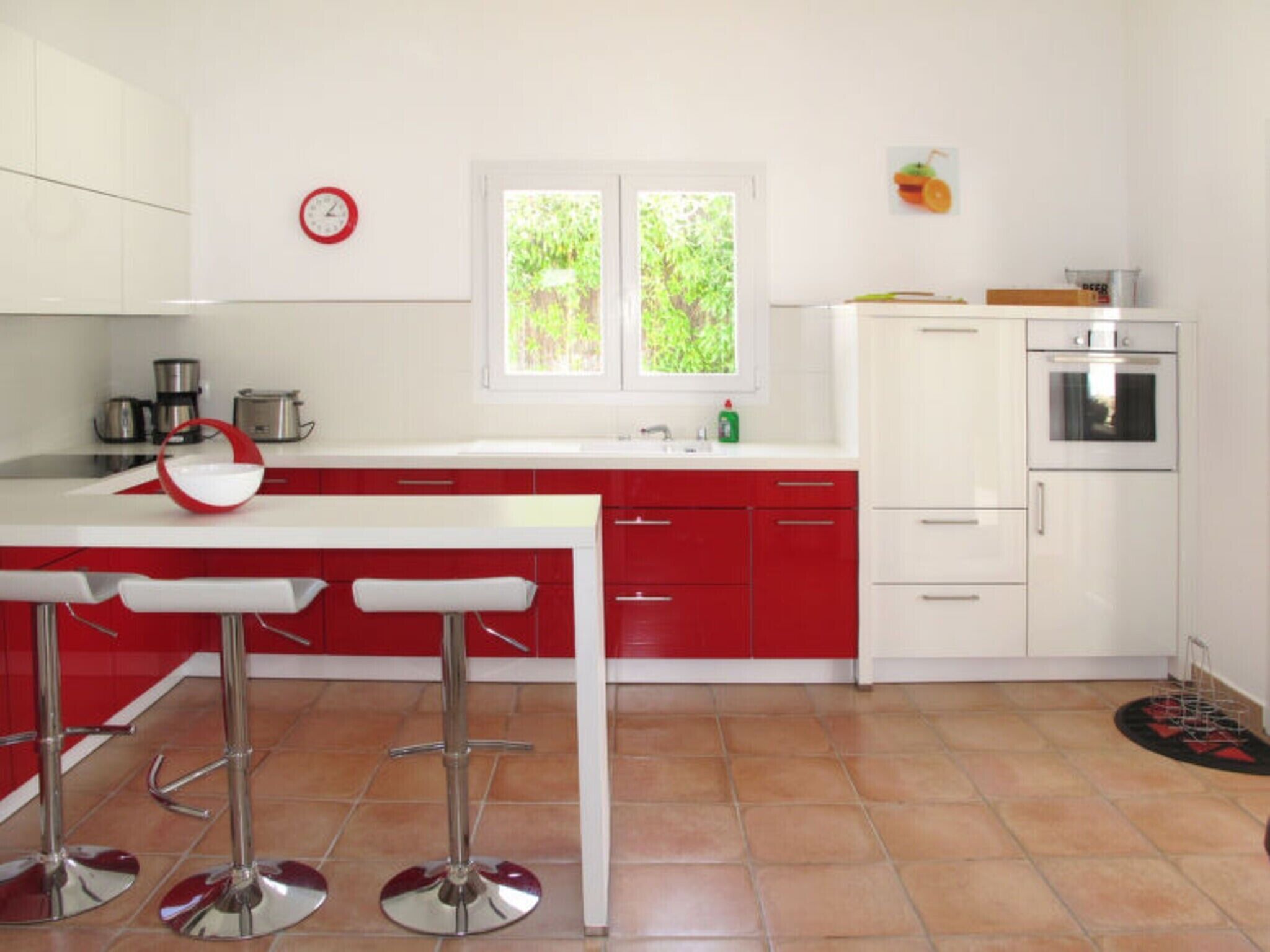 Una cocina moderna con armarios blancos y rojos, un lavamanos de acero inoxidable y un ventanal grande.