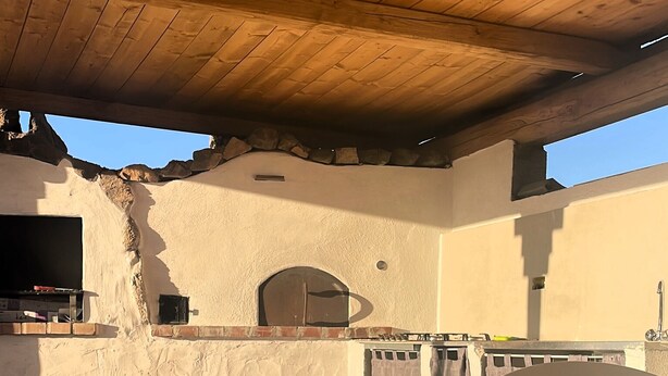 An outdoor patio area with a wooden ceiling, a stone wall, and a view of the sky. - Camere matrimoniali comunicanti (Sardegna)