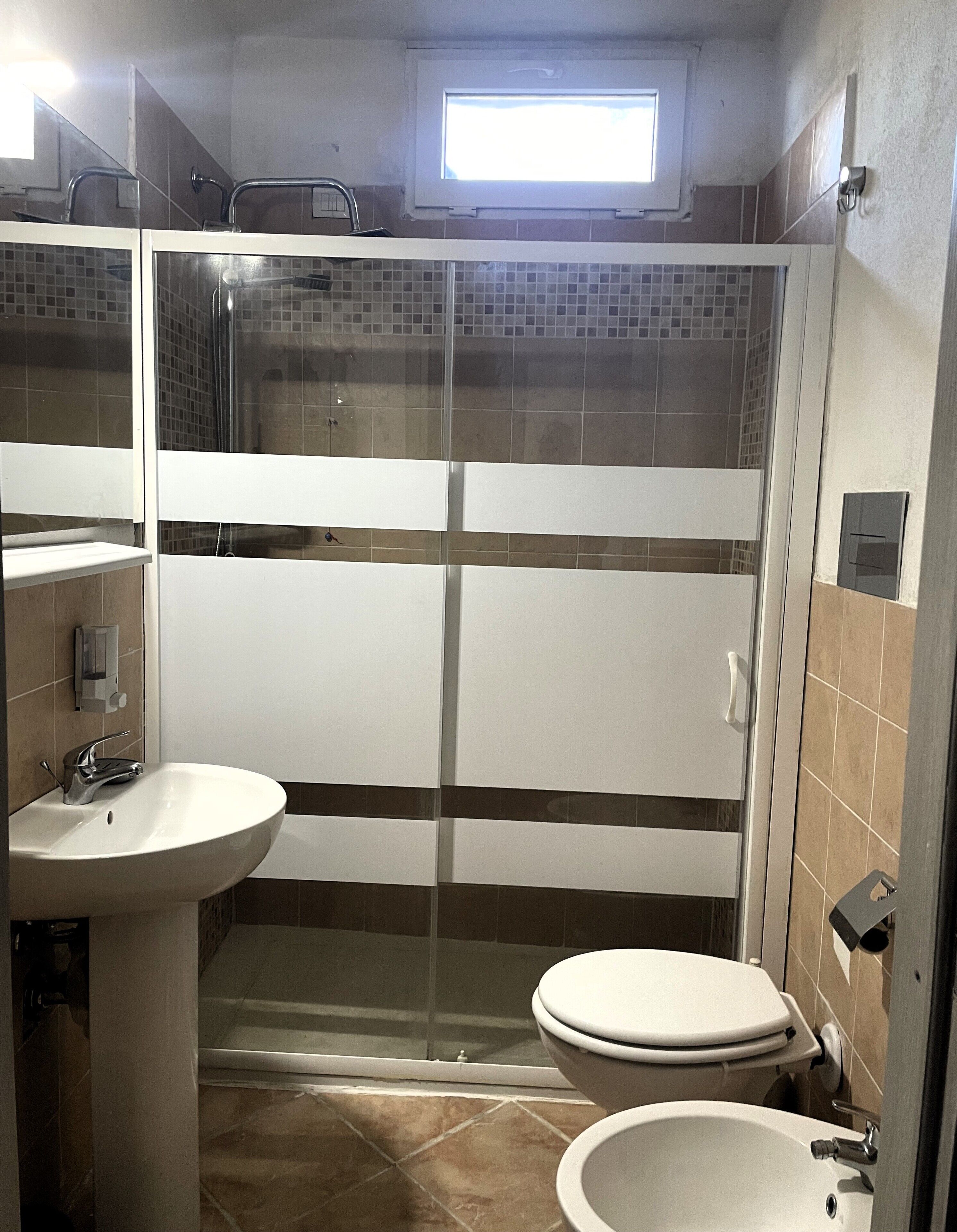 Une salle de bain équipée d’une douche, de toilettes, d’un lavabo et d’une fenêtre située au-dessus de la douche.