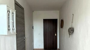 A hallway with a dark wooden door, a white cabinet, and a wall-mounted decorative item. - Camere matrimoniali comunicanti (Sardegna)