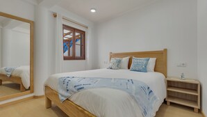 A bedroom with a wooden bed, a bedside table, a mirror, and a window with curtains. - Maiata Beach House 2 (Madeira)