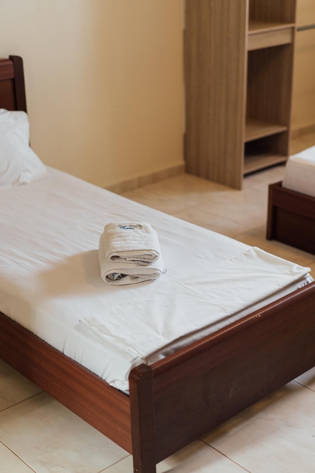 Un letto ben rifatto con un asciugamano piegato, una testiera in legno e un armadio in legno sullo sfondo.
