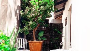 Un pequeño espacio al aire libre con dos sillas y una mesa, rodeado de plantas y un árbol.