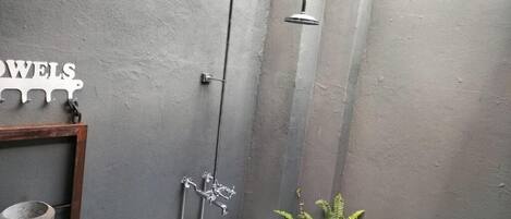 A bathroom with a shower, a towel rack, and a small shelf with a bucket.
