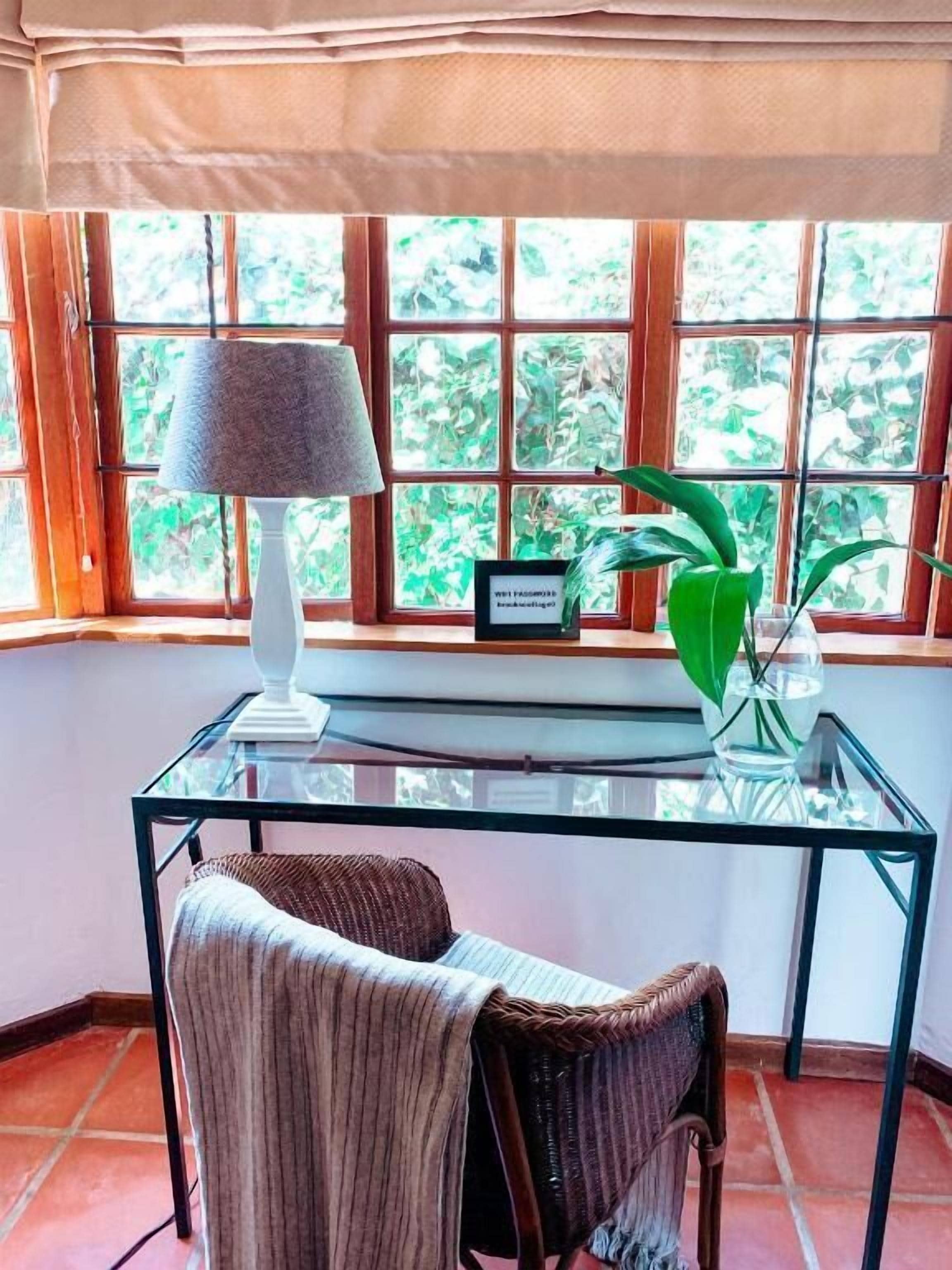 Una habitación con una mesa de vidrio, una silla, una lámpara y una ventana con vistas a zonas verdes.
