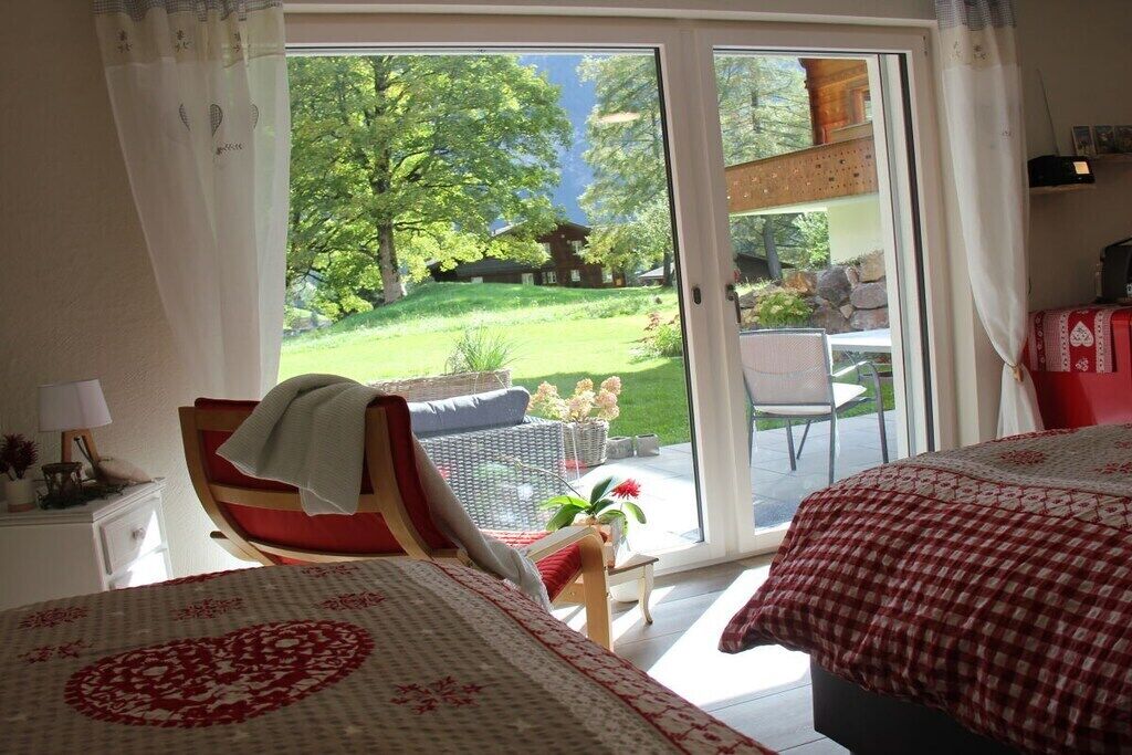 Une chambre à coucher comprenant un lit, une chaise, une table et donnant sur un jardin grâce à une porte coulissante.