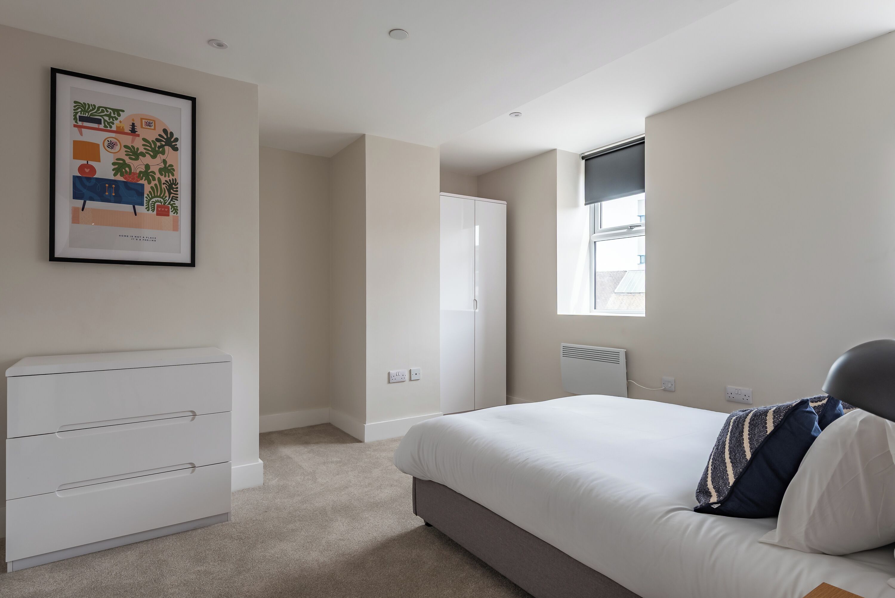 Une chambre à coucher avec un lit, une commode, un tableau encadré au mur et une fenêtre.