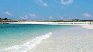 En strand med kristallklart turkosfärgat vatten, vit sand och sparsam växtlighet.