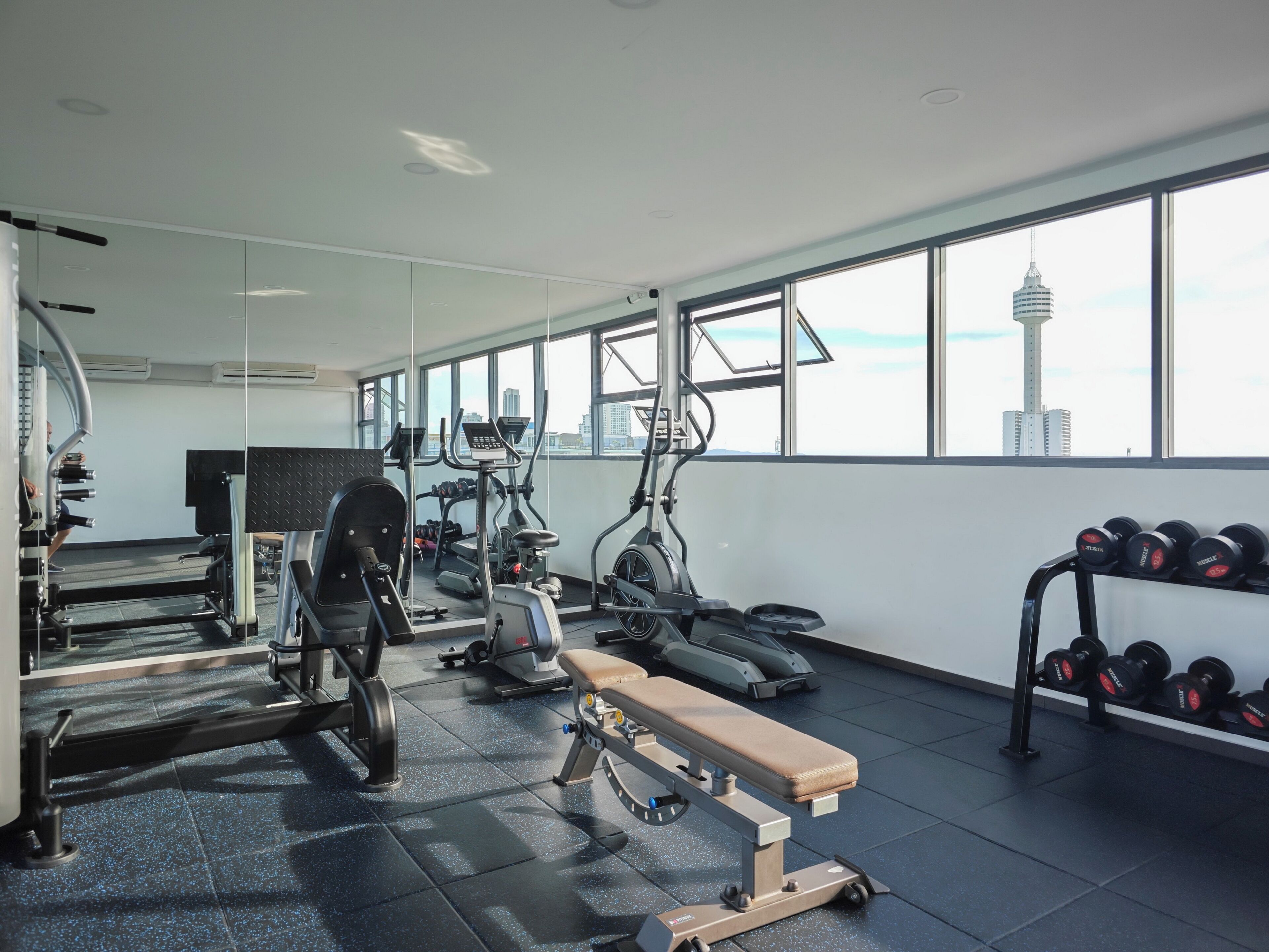A gym with exercise equipment, a bench, and a rack of dumbbells.