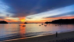 A beach with boats, a person, and a sunset.