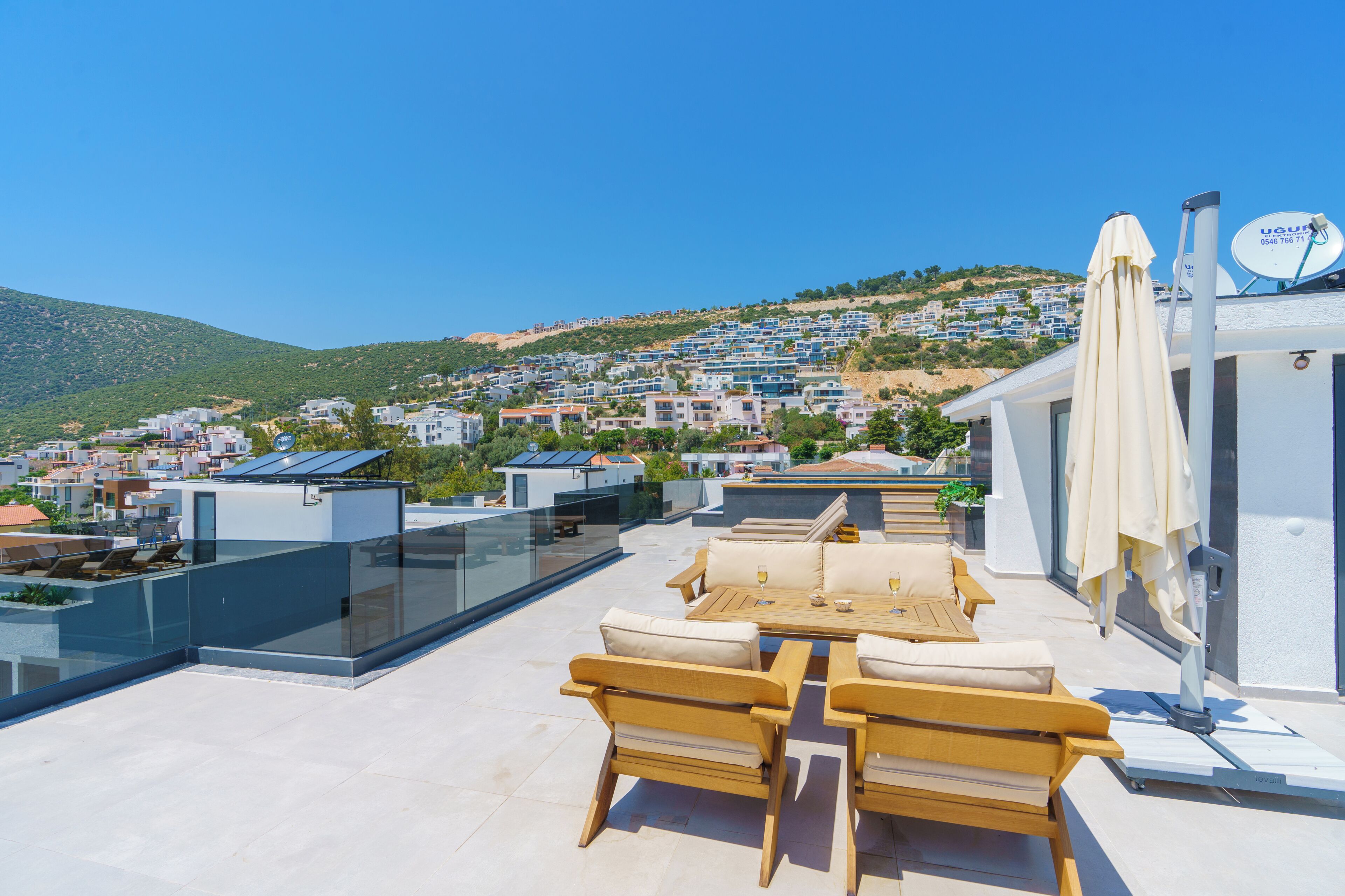 Terraza en la azotea con mobiliario exterior, baranda de vidrio y vistas a un pueblo en la colina.