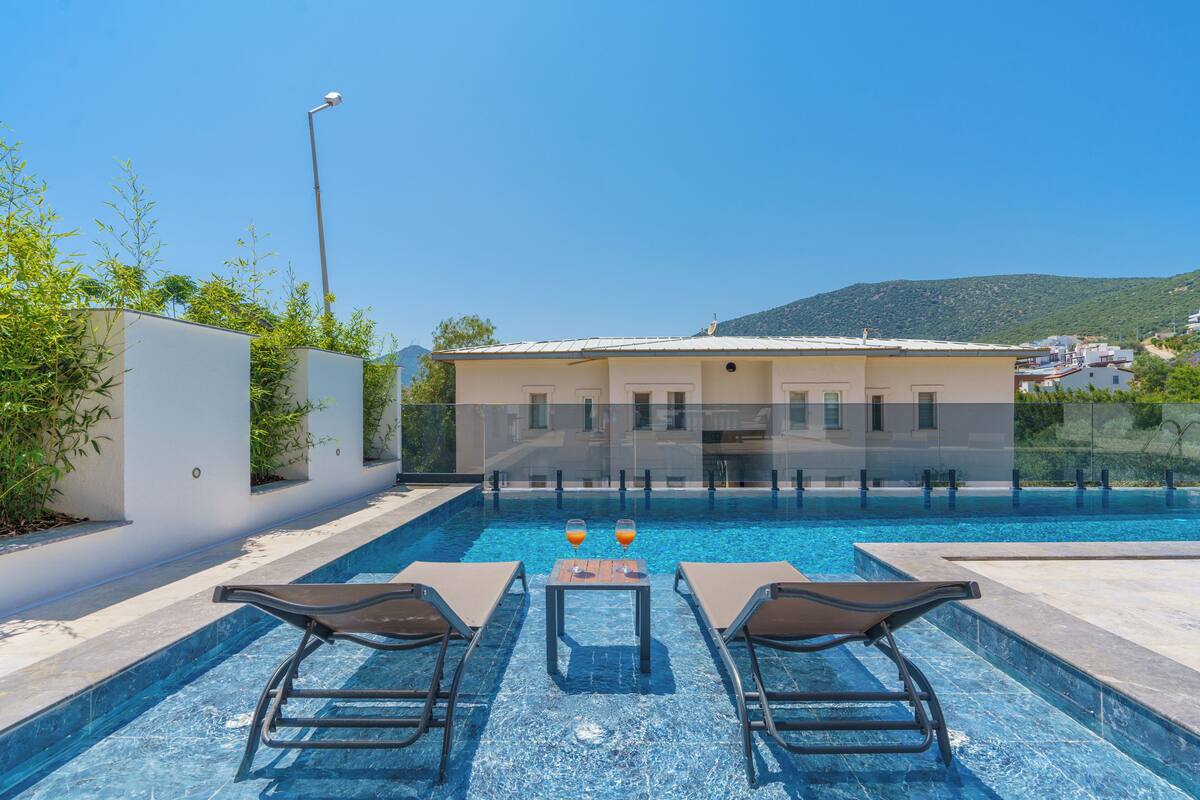 Una piscina con sillas de descanso y una mesa, rodeada por un muro blanco y vegetación.