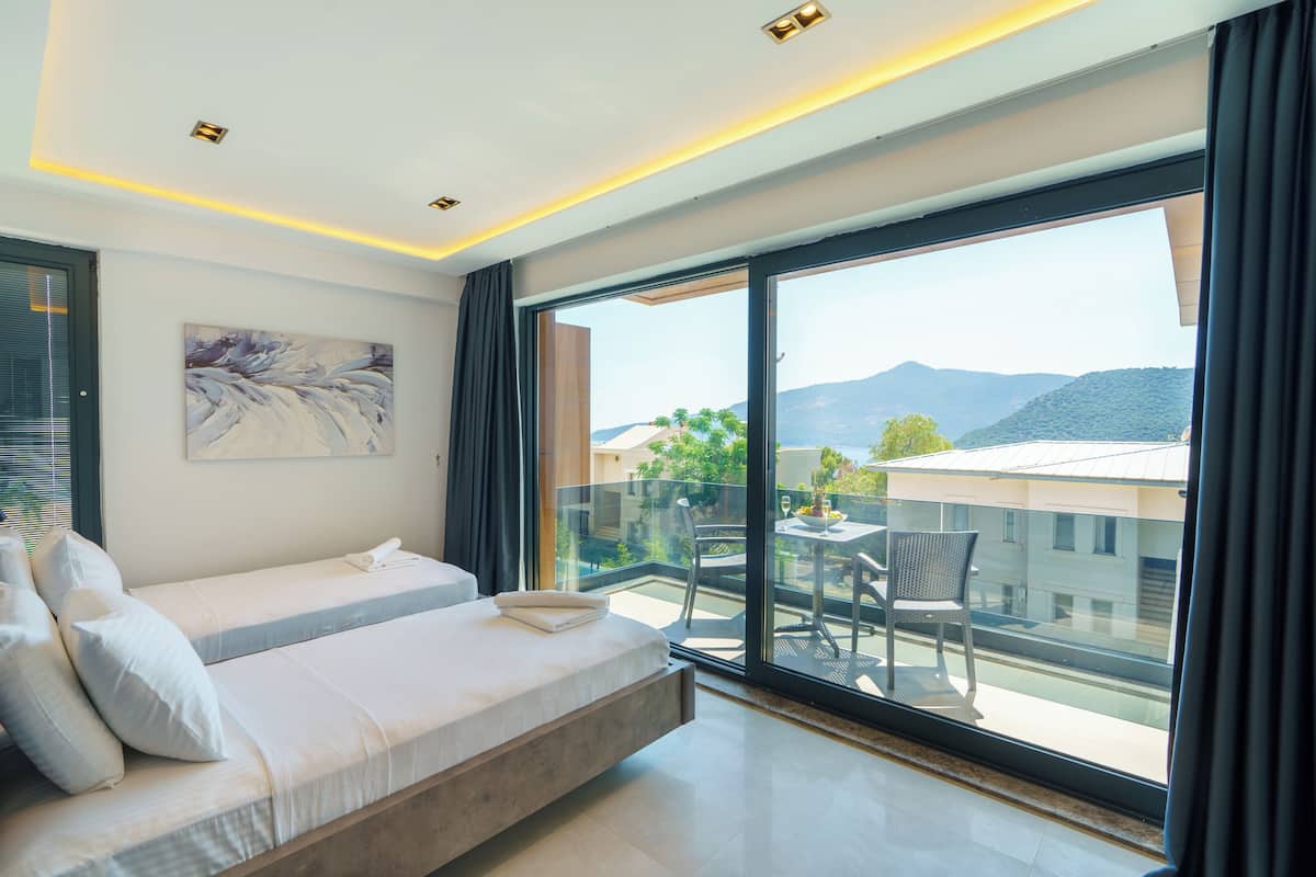 Un dormitorio moderno con una cama grande, un balcón con mesa y sillas, y vistas a la montaña.