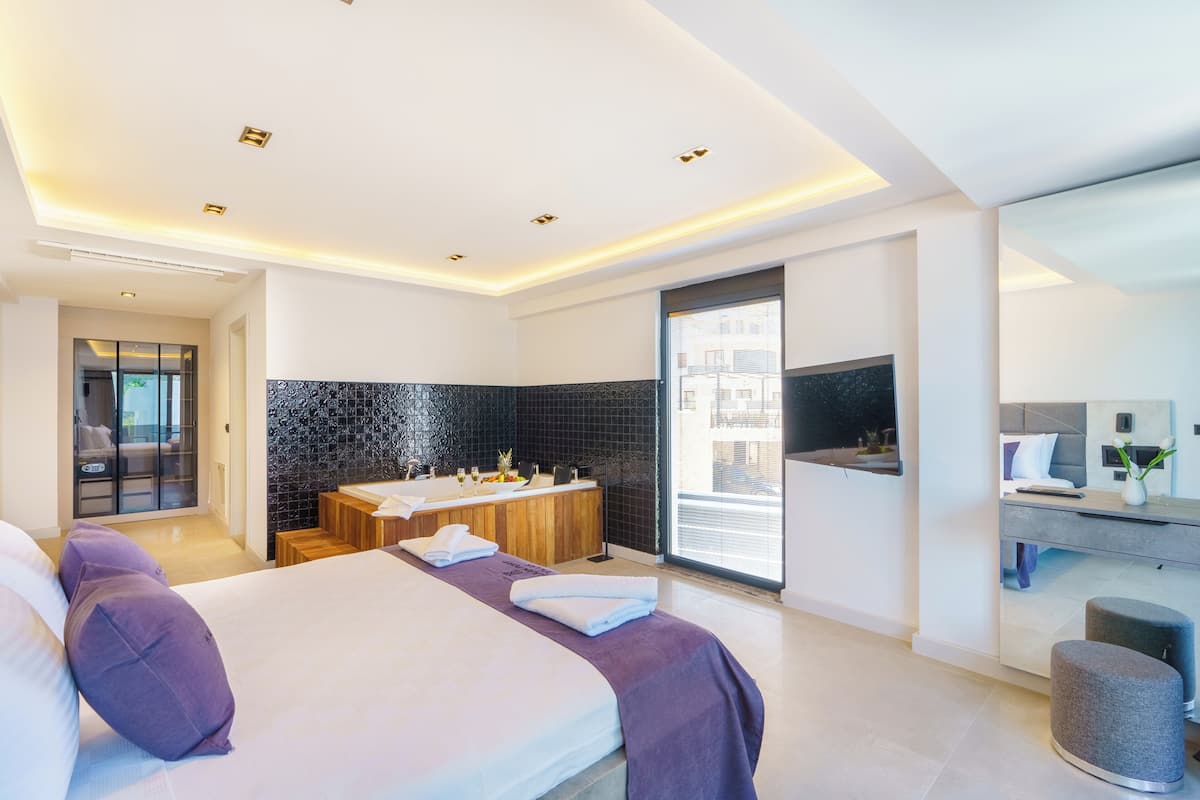 Una habitación de hotel moderna con una cama grande, un baño con bañera, un escritorio y un ventanal amplio.