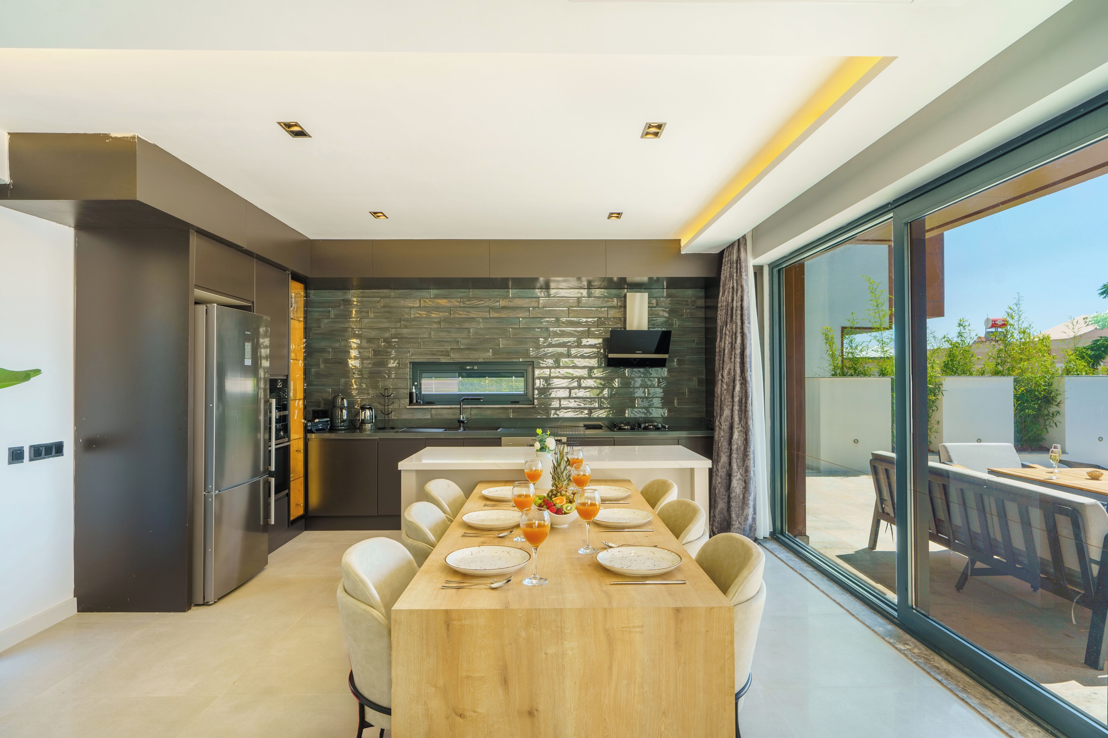 A modern kitchen with a dining area, a built-in oven, and a large window overlooking the outdoor patio.