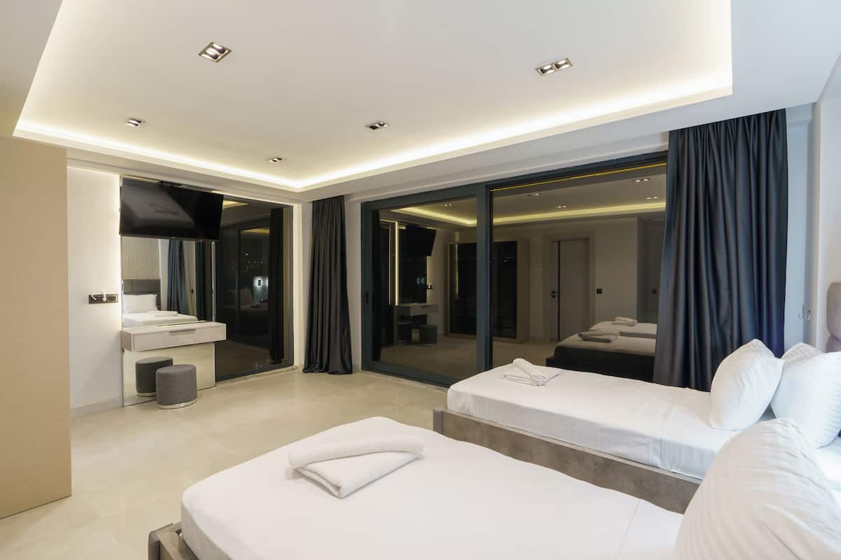 Habitación de hotel moderna con dos camas, baño y un amplio ventanal corredera que da a un balcón.