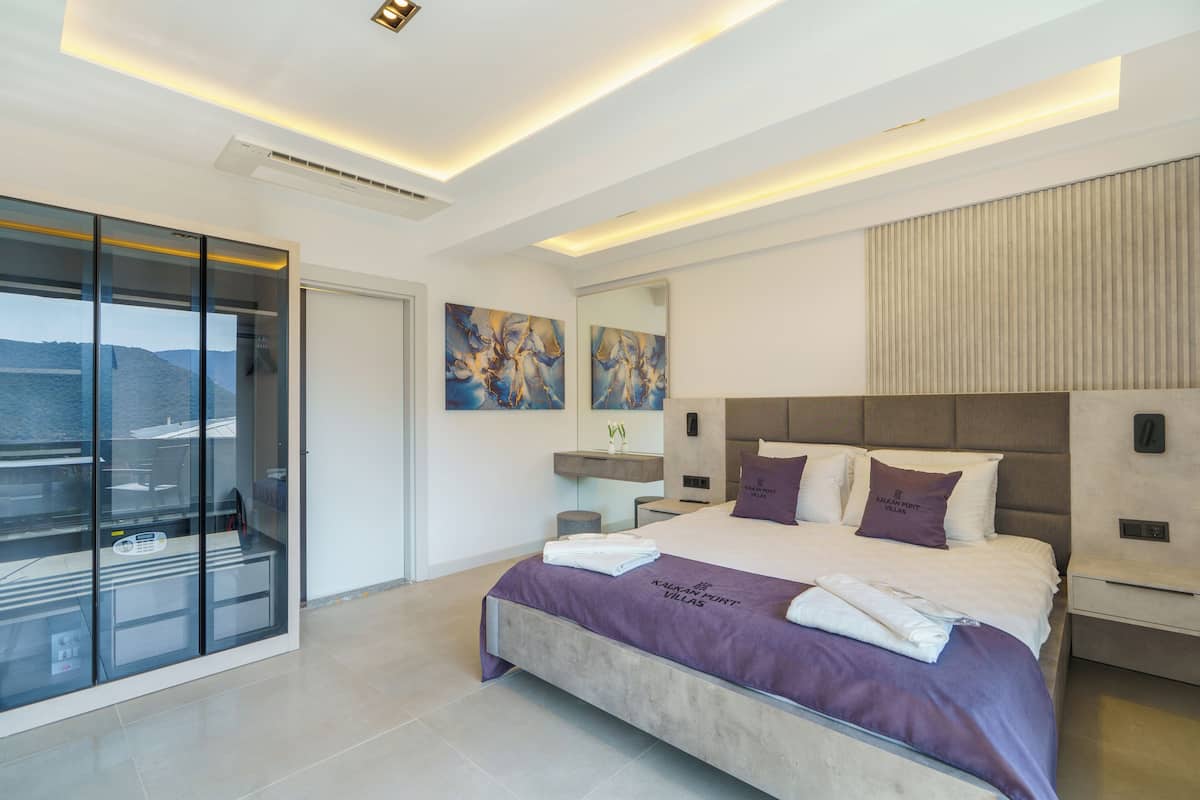 Un dormitorio moderno con una cama grande, un ventanal de vidrio que da a un balcón y obras de arte en las paredes.