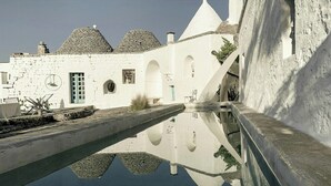 A courtyard with a reflective pool, white buildings with stone roofs, and arched doorways. - Designer trullo in Valle d'Itria, Apulia (Cisternino)