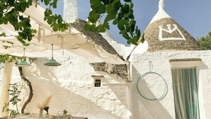 A white-walled building with a conical roof, a table with chairs, and hanging lamps. - Designer trullo in Valle d'Itria, Apulia (Cisternino)