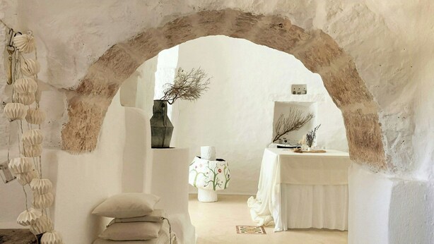 An arched doorway leading to a room with a white table, a vase with branches, and a wall-mounted light fixture. - Designer trullo in Valle d'Itria, Apulia (Cisternino)