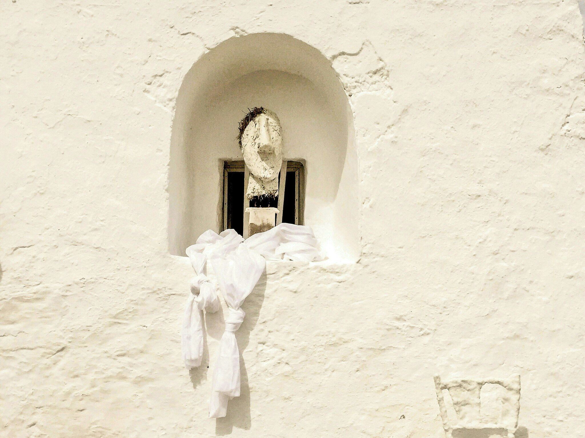 Un bâtiment blanc avec une petite fenêtre en arc de cercle et un tissu blanc suspendu devant.