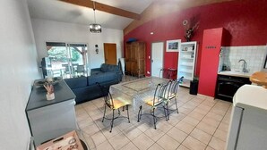A spacious living area with a dining table and chairs, a sofa, and a kitchen area with a red accent wall. - Apartment*Residence with pool*Parking*3 min from downtown Sarlat (Sarlat-la-Canéda)