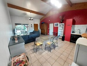 Un vaste espace de vie comprenant une table à manger et des chaises, un canapé et un coin cuisine agrémenté d’un mur d’accent rouge.