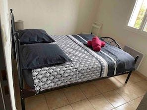 Un lit simple avec une couvre-lit à motifs, deux oreillers et un objet rouge sur le lit.