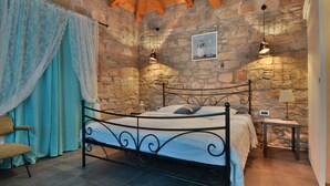 Une chambre avec un mur en pierre, un cadre de lit en métal, une table de chevet avec une lampe et une chaise.