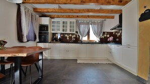 Une cuisine avec des meubles blancs, une table à manger en bois et une fenêtre avec des rideaux.