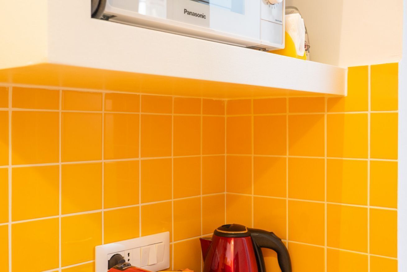 Una cucina con piastrelle arancioni, un bollitore rosso e un forno a microonde Panasonic.