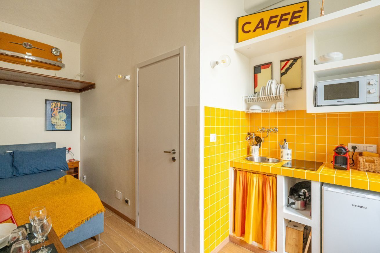 Une pièce comprenant un lit, une petite table avec des verres, un four à micro-ondes et un évier dans un coin cuisine.