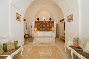 Quarto com cama, duas mesas de cabeceira, um criado-mudo, tapete estampado e um painel decorativo na parede.