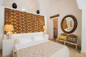 A hotel room with a patterned headboard, a large mirror, a bed with white linens, a bedside table with a lamp, and a bench with cushions. - Historic gem with antiques & private pool (Santa Cesarea Terme)