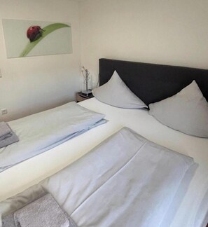 A double bed with white linens, a nightstand with a lamp, and a wall-mounted picture of a flower. - moderne Wohnung in Willingen (Willingen)