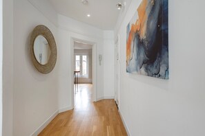 Een gang met een houten vloer, een ronde spiegel en een groot abstract schilderij aan de muur.