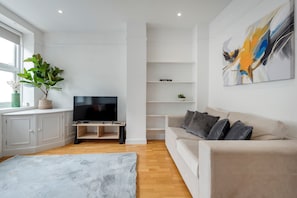Een moderne woonkamer met een flatscreentelevisie, een beige bank, een groot abstract schilderij en een potplant.