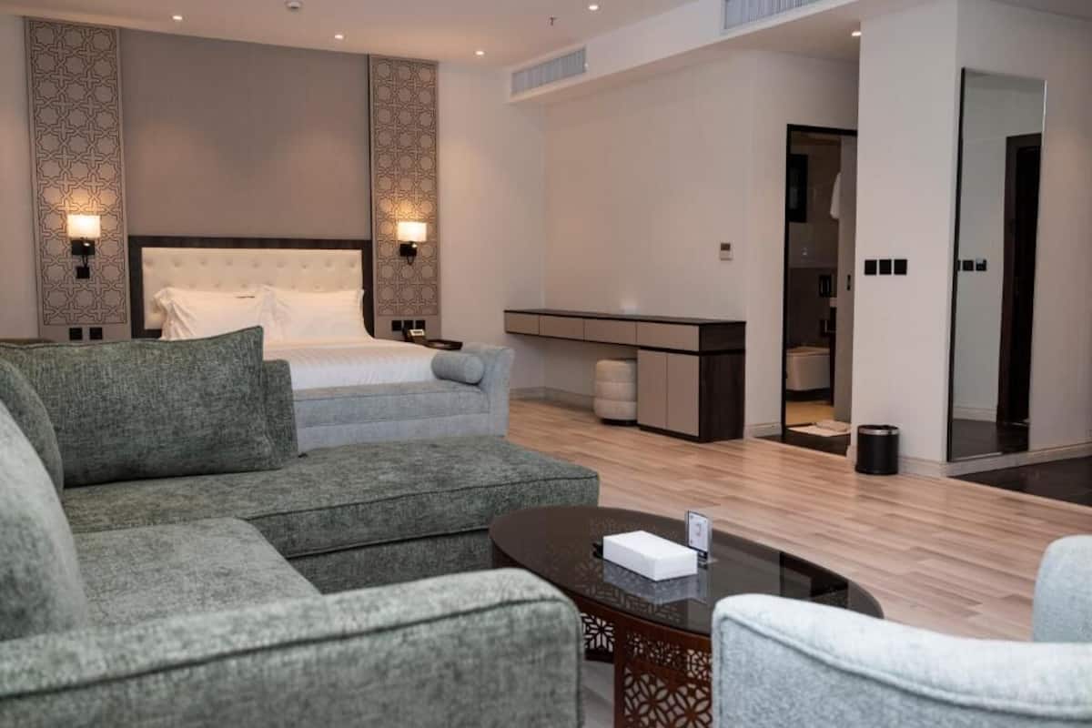 Ett modernt hotellrum med en stor säng, grå stoppade soffor, ett litet bord och ett inbyggt skrivbord med en spegel.