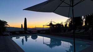 Une piscine offrant une vue dégagée sur le coucher de soleil, entourée de chaises longues et agrémentée d’une pergola.