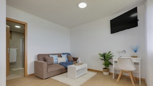 Ein modernes Wohnzimmer mit Sofa, Couchtisch, Fernseher, Schreibtisch, Sessel und Blumentöpfen.