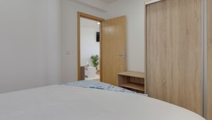 Ein Schlafzimmer mit einem Bett, einem Holzschrank, einem kleinen Holzregal und einer Tür zu einem anderen Raum.