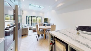 A modern kitchen with a marble countertop, a dining area with a round table and chairs, and a large window providing natural light. - Prime 3BR Flat With Private Patio-Walk to Tube (Richmond)