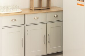 A kitchen with white cabinets, a wooden countertop, and a glass tray with glasses. - Simple House (Santa Maria di Leuca)