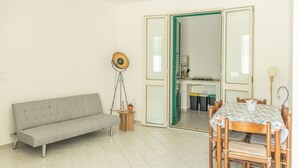 Een kamer met een bank, een eettafel met stoelen, een lamp en een deur naar een andere kamer.