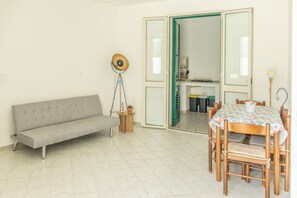 A room with a sofa, a dining table with chairs, a lamp, and a door leading to another room. - Simple House (Santa Maria di Leuca)