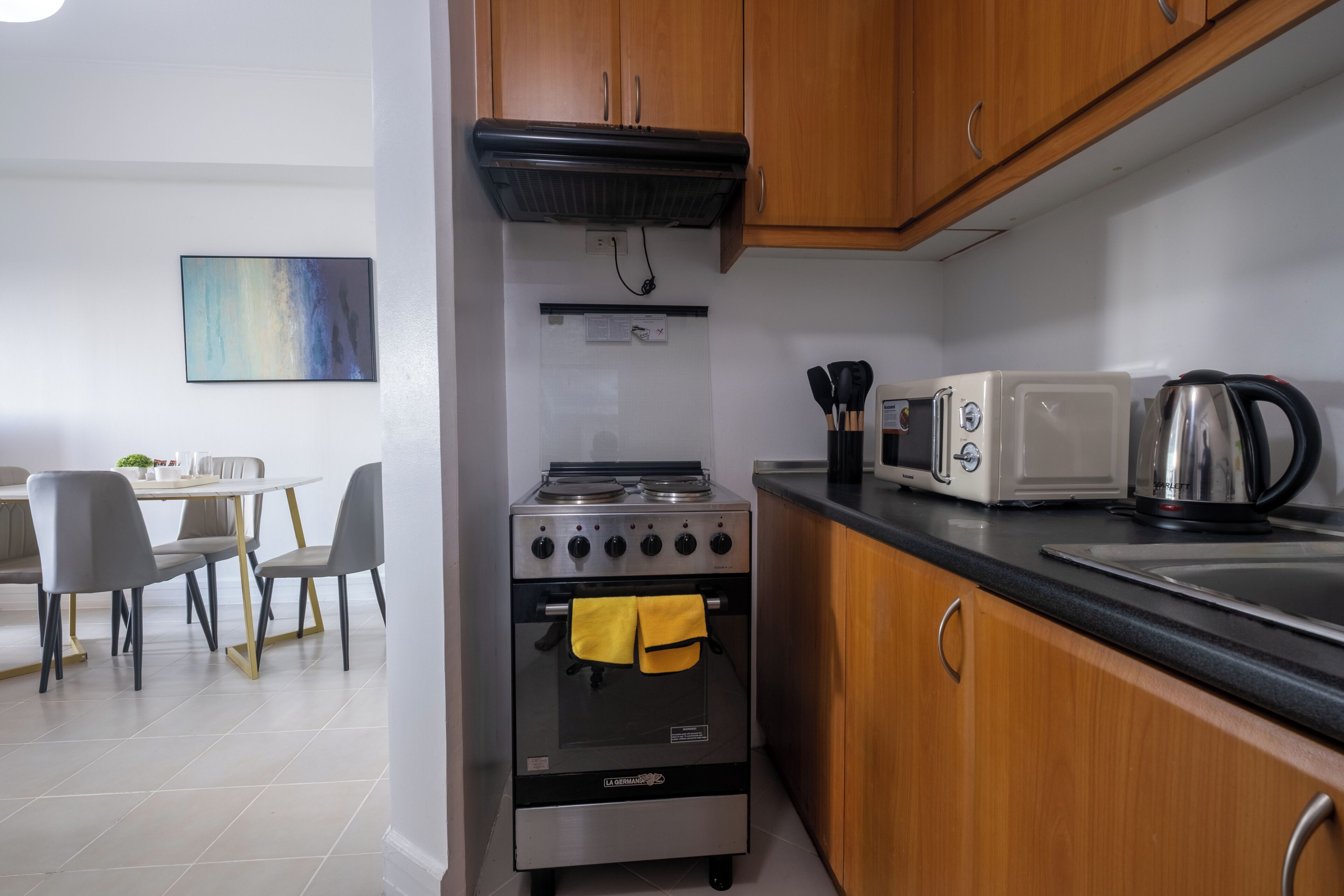 A compact kitchen with a stove, oven, microwave, and kettle. There is a dining area with chairs and a table.