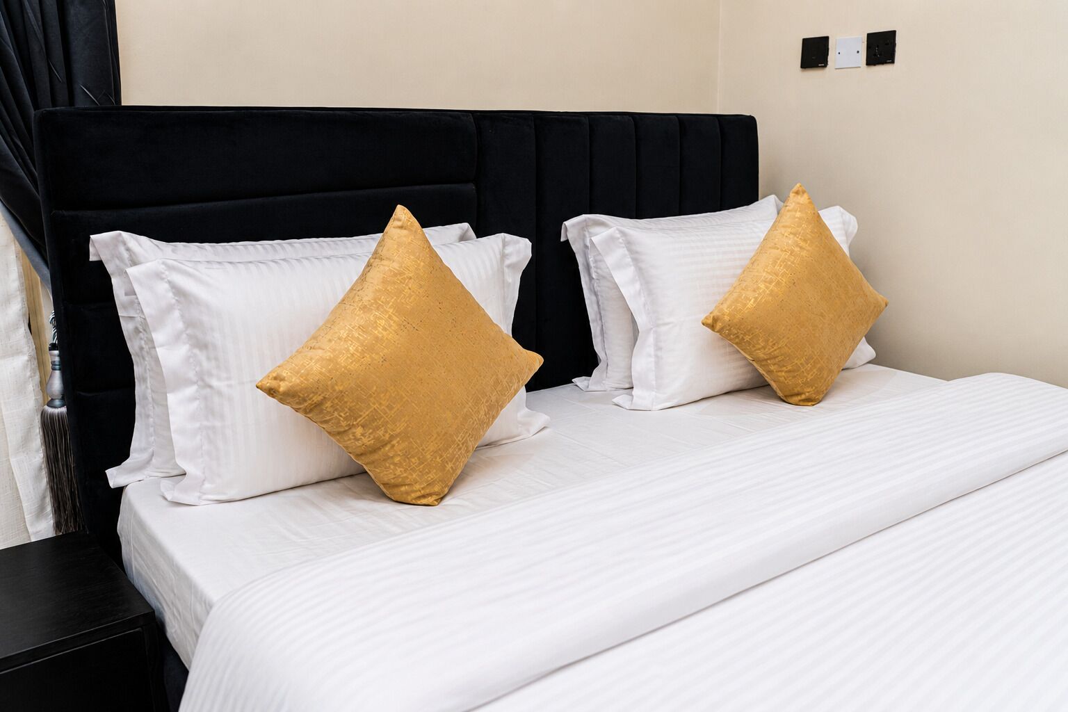 A bed with white bedding and two gold pillows, a black headboard, and a black nightstand.